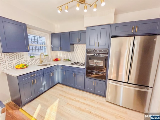 kitchen featuring stainless steel appliances, a sink, light wood-style floors, light countertops, and a warming drawer