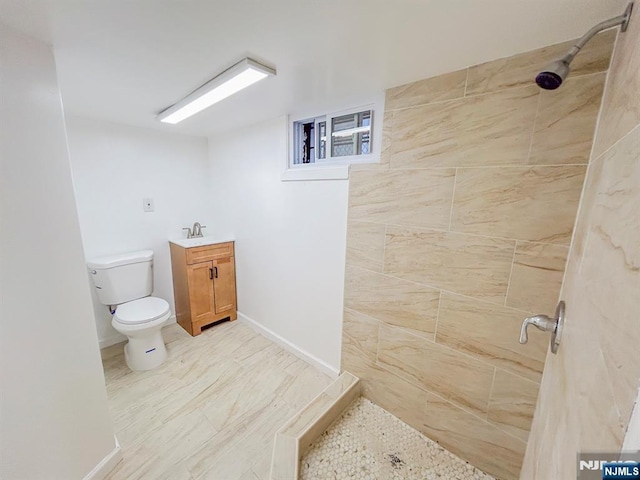 full bath featuring vanity, a tile shower, toilet, and baseboards