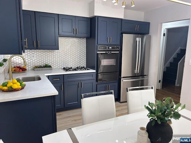 kitchen featuring blue cabinets, stainless steel appliances, a sink, light countertops, and a warming drawer