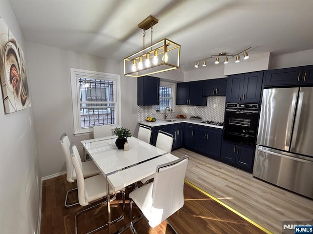 kitchen with backsplash, freestanding refrigerator, a sink, wood finished floors, and black oven