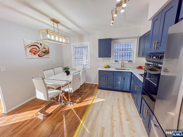 kitchen featuring decorative backsplash, light wood-type flooring, blue cabinetry, a sink, and black oven