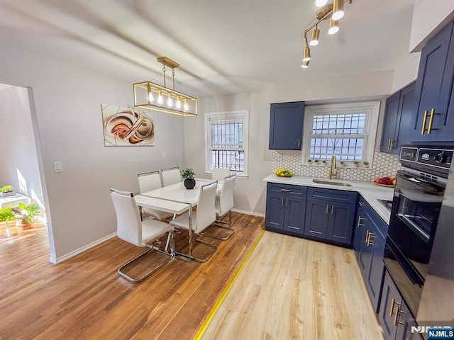 kitchen with blue cabinets, a sink, light countertops, backsplash, and black oven