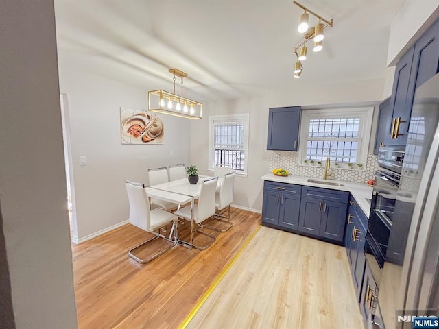 kitchen with tasteful backsplash, blue cabinetry, light countertops, light wood-style floors, and a sink