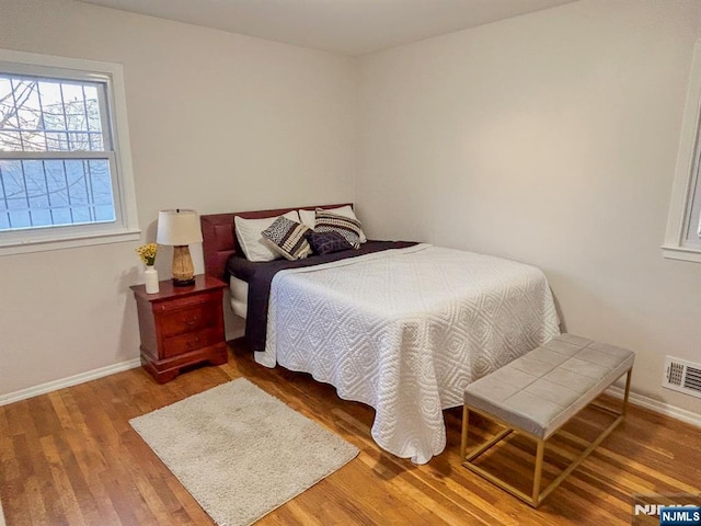 bedroom with baseboards, visible vents, and wood finished floors