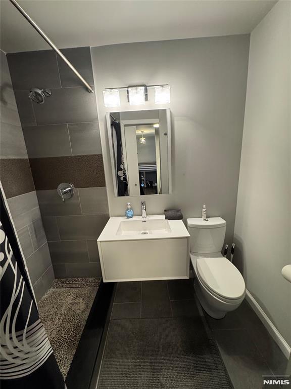 full bath with toilet, vanity, baseboards, a tile shower, and tile patterned floors