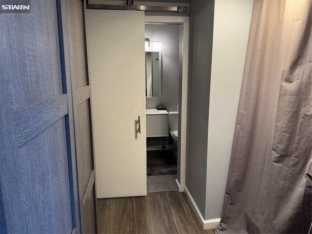 corridor with a barn door, dark wood finished floors, and baseboards