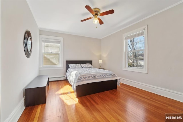 bedroom featuring wood-type flooring, multiple windows, a baseboard heating unit, and baseboards