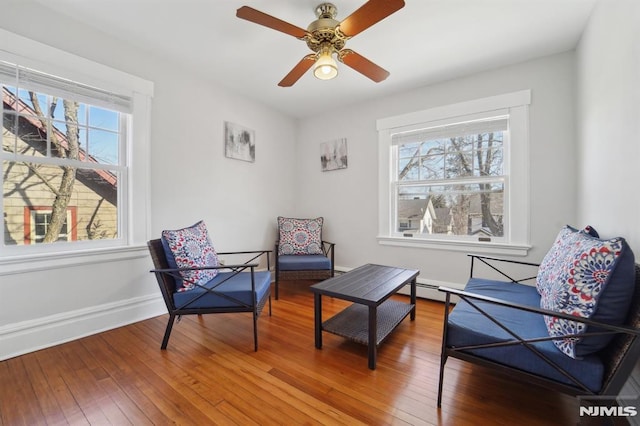 living area featuring wood-type flooring, plenty of natural light, baseboards, and ceiling fan