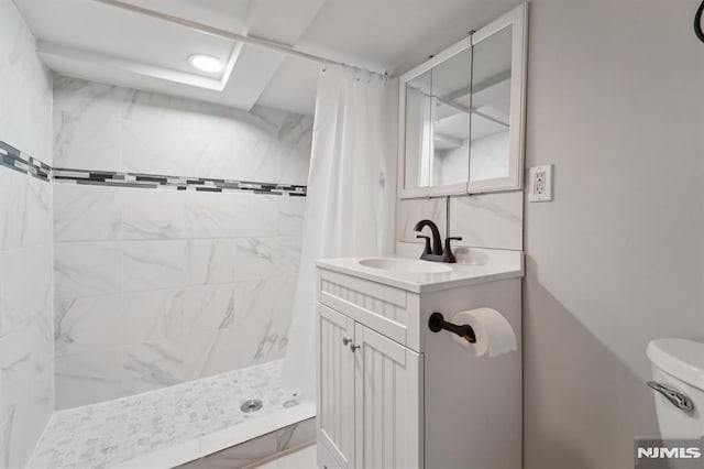 bathroom with tiled shower, vanity, and toilet