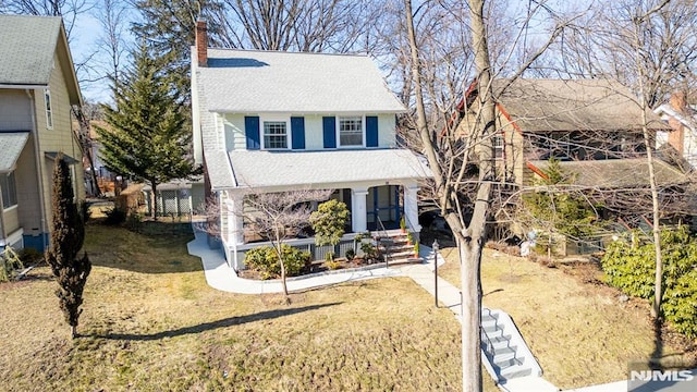 view of front of property with covered porch, a chimney, and a front lawn