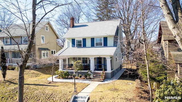 view of front of house with covered porch, roof with shingles, a chimney, and a front yard