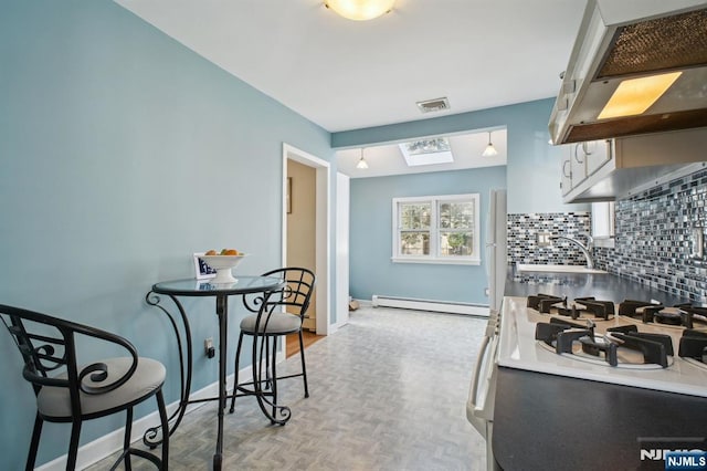 kitchen with visible vents, backsplash, baseboard heating, under cabinet range hood, and a sink