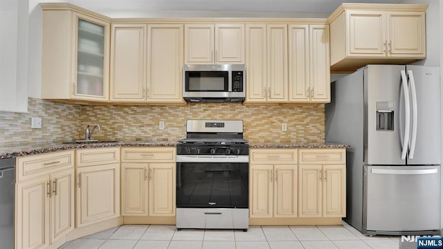 kitchen with stainless steel appliances, dark stone countertops, a sink, and cream cabinets