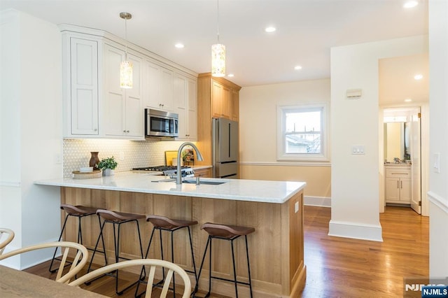 kitchen featuring stainless steel appliances, light countertops, a sink, and a peninsula