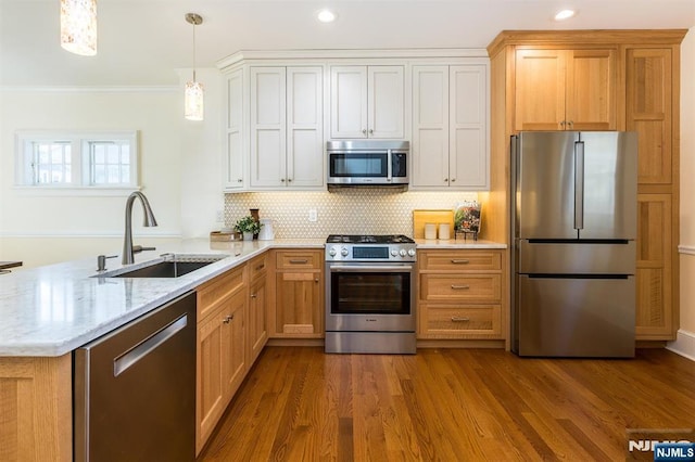 kitchen featuring a peninsula, a sink, appliances with stainless steel finishes, dark wood finished floors, and crown molding