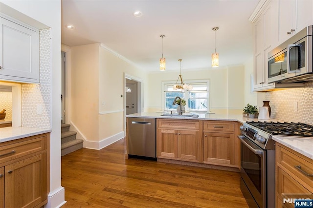 kitchen with stainless steel appliances, a peninsula, dark wood-style flooring, a sink, and decorative backsplash