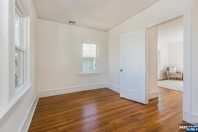 spare room featuring wood-type flooring, visible vents, and baseboards