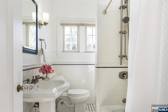 bathroom featuring toilet, wainscoting, shower / bath combination with curtain, and tile walls