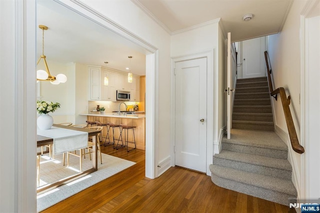 stairs with a chandelier, ornamental molding, and wood finished floors