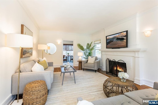 living room with a warm lit fireplace, baseboards, ornamental molding, and light wood-style floors