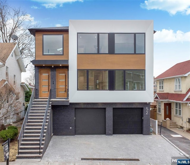 contemporary house with a garage, brick siding, stairs, decorative driveway, and stucco siding