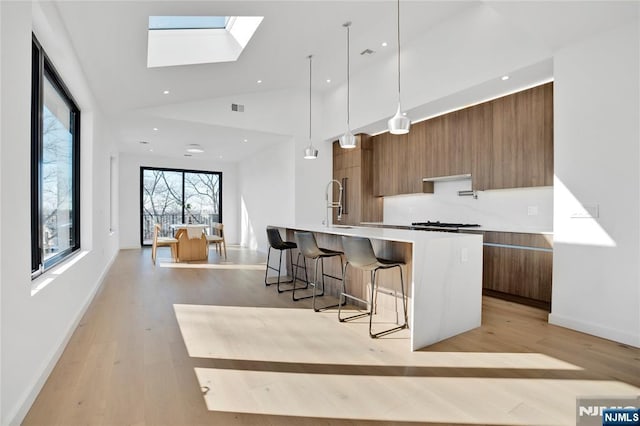 kitchen featuring a breakfast bar, a spacious island, light countertops, brown cabinetry, and modern cabinets