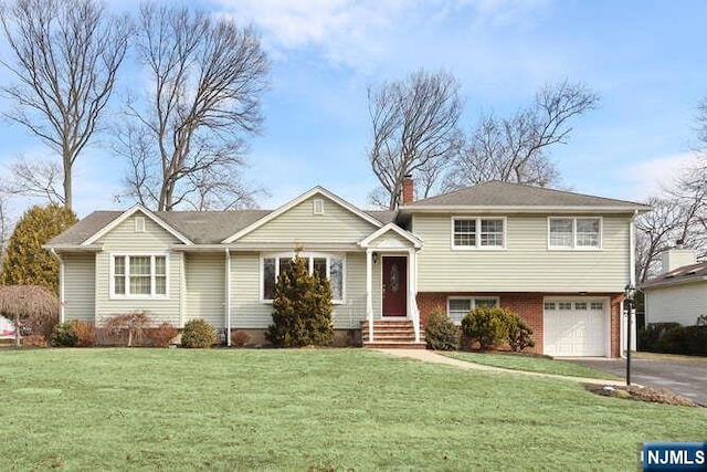 tri-level home with a garage, brick siding, driveway, a chimney, and a front yard