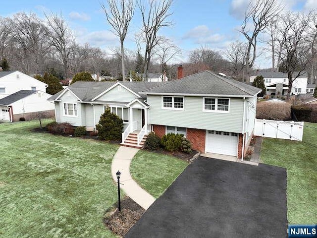 tri-level home featuring a chimney, aphalt driveway, a gate, a front lawn, and brick siding