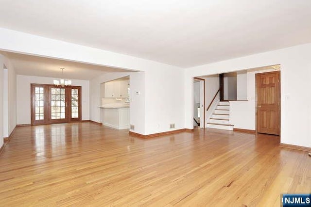 unfurnished living room featuring light wood-style floors, stairway, baseboards, and an inviting chandelier