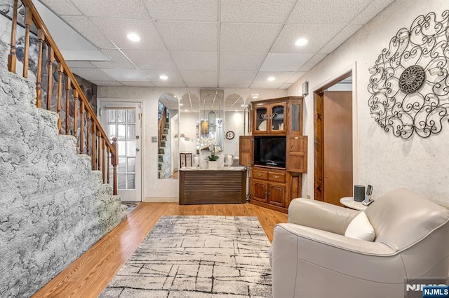 living area featuring arched walkways, a drop ceiling, recessed lighting, stairs, and light wood-type flooring