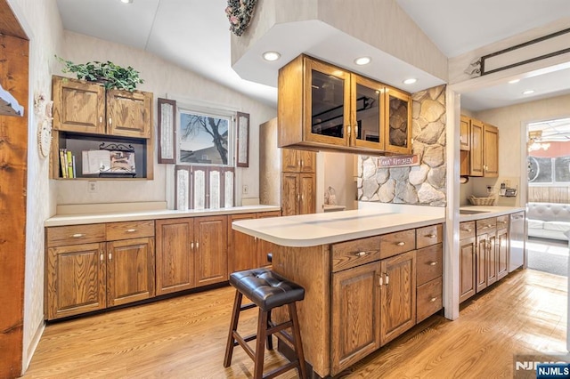 kitchen with dishwasher, lofted ceiling, brown cabinets, light countertops, and light wood-style floors