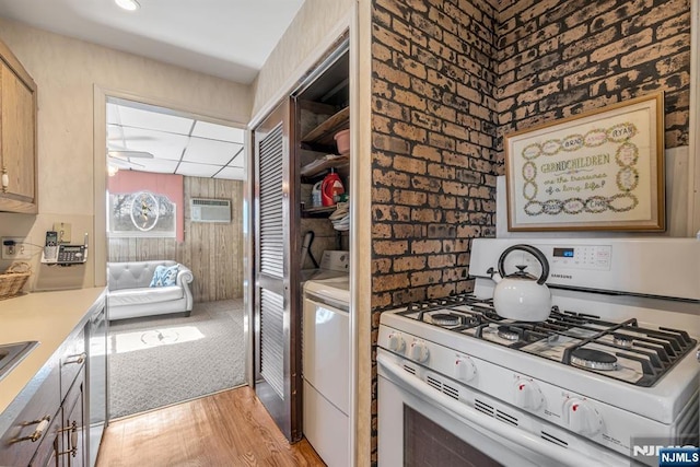 kitchen featuring white gas range oven, a wall unit AC, light countertops, light wood-style floors, and separate washer and dryer