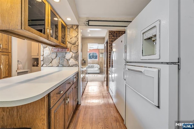 kitchen with light wood-style flooring, glass insert cabinets, brown cabinets, and light countertops