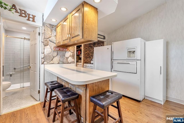 kitchen with a peninsula, light wood finished floors, a kitchen breakfast bar, and freestanding refrigerator