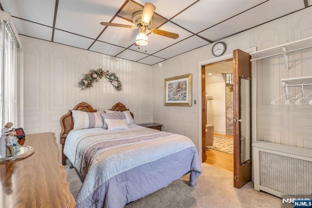 bedroom featuring a paneled ceiling, radiator heating unit, a ceiling fan, light carpet, and connected bathroom