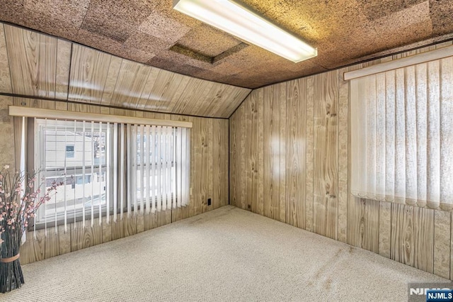 carpeted spare room featuring lofted ceiling, wooden ceiling, and wooden walls