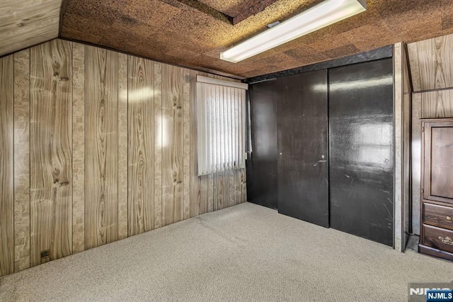 unfurnished bedroom with lofted ceiling, wood walls, and carpet flooring