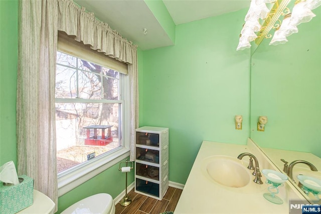 half bathroom with wood finish floors, vanity, toilet, and baseboards