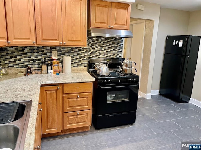 kitchen featuring under cabinet range hood, a sink, baseboards, backsplash, and black appliances