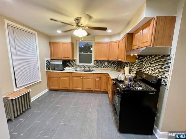 kitchen with radiator, light countertops, black range with gas cooktop, a sink, and under cabinet range hood