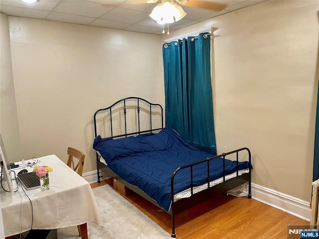 bedroom featuring baseboards, a drop ceiling, and wood finished floors