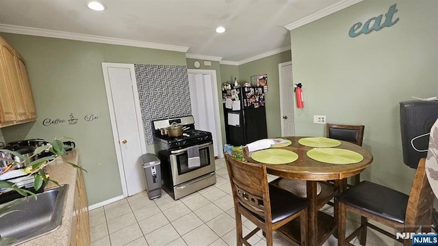 kitchen with light tile patterned floors, ornamental molding, stainless steel range with gas stovetop, freestanding refrigerator, and a sink