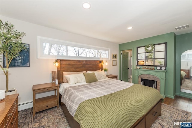 bedroom featuring visible vents, a baseboard radiator, wood finished floors, a fireplace, and recessed lighting