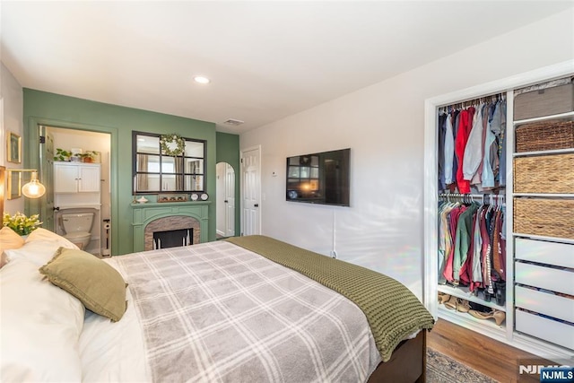 bedroom with arched walkways, connected bathroom, wood finished floors, a closet, and recessed lighting