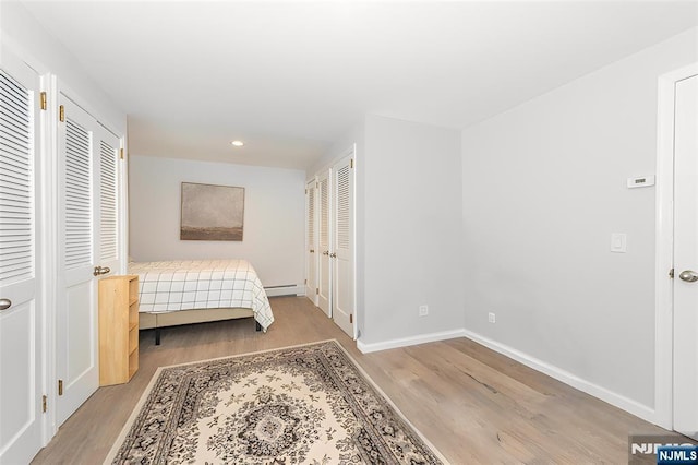 bedroom featuring baseboards, wood finished floors, a baseboard heating unit, multiple closets, and recessed lighting