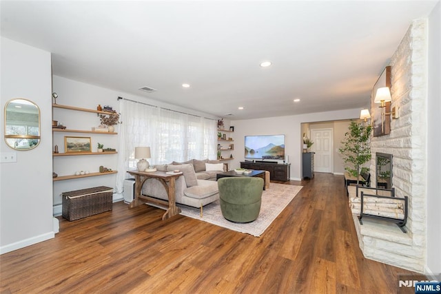 living room with a stone fireplace, recessed lighting, wood finished floors, visible vents, and baseboards