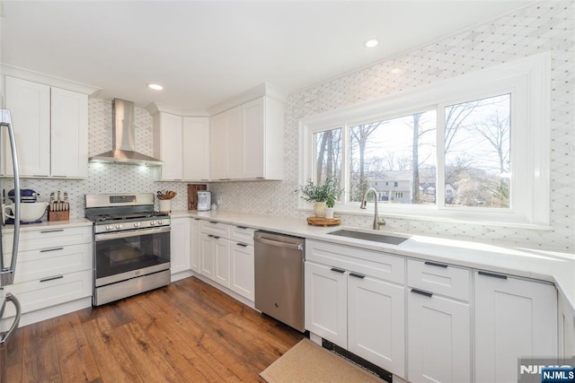 kitchen with wall chimney exhaust hood, appliances with stainless steel finishes, dark wood-type flooring, white cabinetry, and a sink