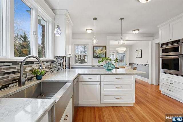 kitchen featuring double oven, white cabinets, a peninsula, and decorative backsplash