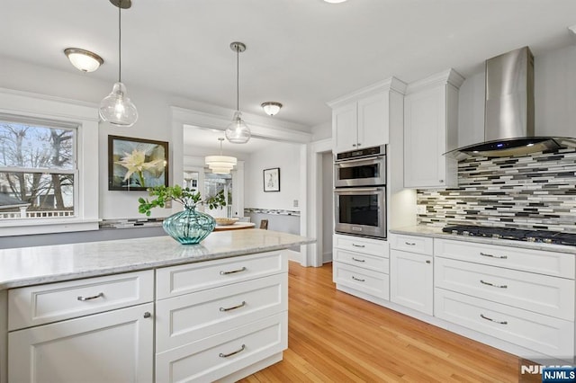 kitchen featuring stainless steel appliances, decorative backsplash, light wood-style floors, white cabinets, and wall chimney range hood