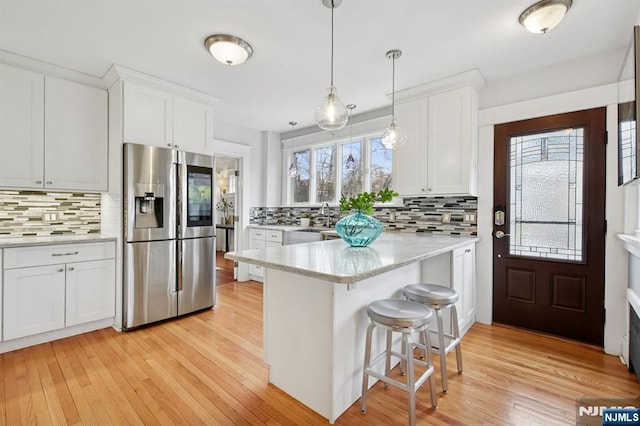 kitchen featuring stainless steel refrigerator with ice dispenser, light countertops, white cabinetry, light wood-type flooring, and a peninsula